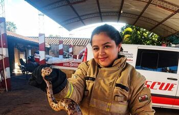 Mujer bombero sonriente con uniforme beige y guantes oscuros, sosteniendo una serpiente en una escena de rescate.