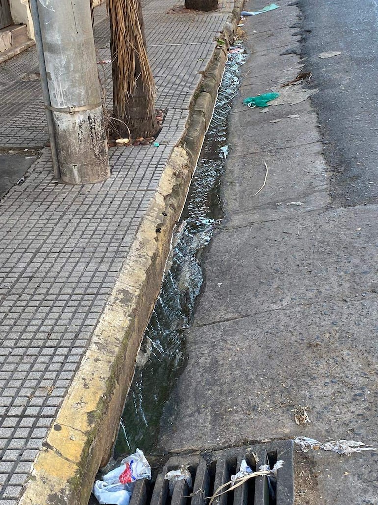 Escena urbana en la calle Tte. Fariña con acera, drenaje y basura acumulada; no hay personas visibles.