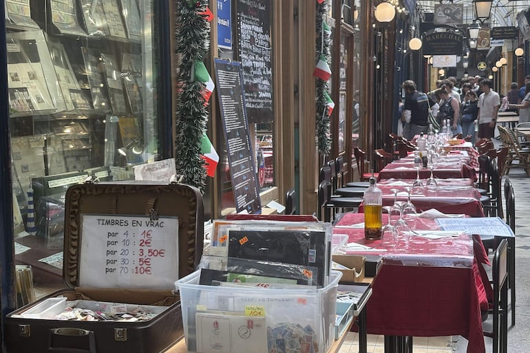Venta de sellos frente a las mesas de un restaurante italiano junto a una aglomeración de turistas al fondo en los Panoramas, París.