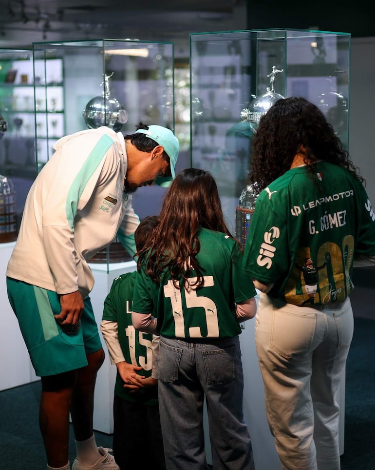 G. Gómez interactúa con una niña en camisetas verdes, rodeados de trofeos en un ambiente de admiración.