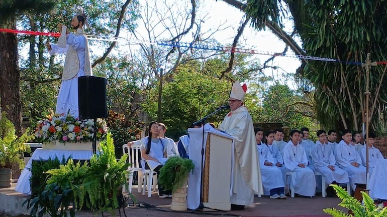 Monseñor Osmar López en atuendo ceremonial habla desde un podio, rodeado de jóvenes con túnicas blancas escuchando atentamente.