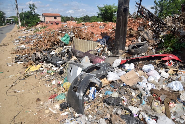 Escena desordenada con basura y escombros. Vegetación dispersa y calles pavimentadas en un entorno urbano descuidado.