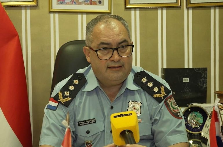 Julio Maldonado, en uniforme azul claro y gafas, habla sentado en su escritorio frente a un micrófono amarillo