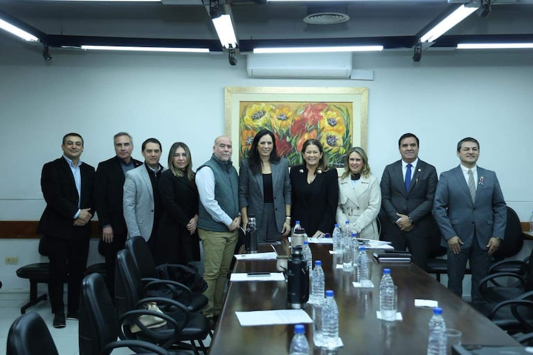 Claudia Centurión y Facundo Salinas en reunión formal, rodeados de hombres y mujeres vestidos de traje en ambiente serio.