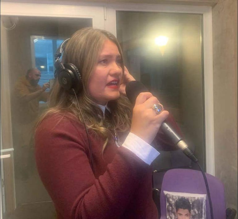 Shirley Giménez con suéter marrón y auriculares, hablando frente a un micrófono en un estudio de grabación.