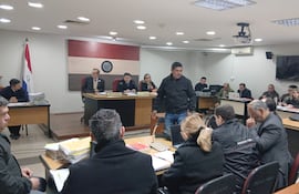 Leonardo Benítez en sala de justicia, vestido con chaqueta oscura, observando atentamente en un ambiente formal con documentos sobre la mesa.