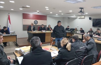 Leonardo Benítez en sala de justicia, vestido con chaqueta oscura, observando atentamente en un ambiente formal con documentos sobre la mesa.