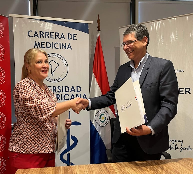 Cecilia Lezcano sonríe mientras estrecha la mano de Hermann Weisensee, en un ambiente formal con carteles de la carrera de Medicina.