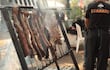 Hombre de espaldas con camiseta 'I ❤️ ASADO' asando carne al aire libre rodeado de humo y ambiente festivo.