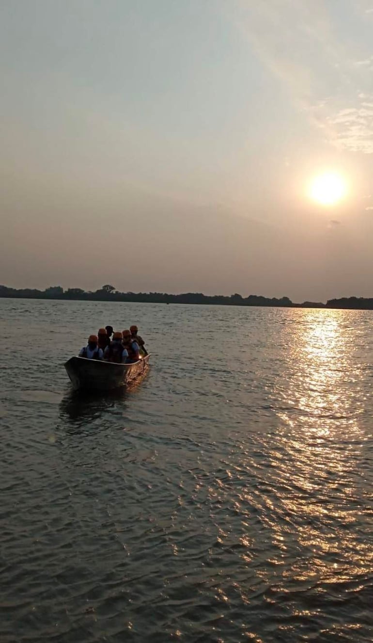 Ocho personas en canoa con cascos amarillos, rodeadas de agua y un hermoso atardecer en el horizonte.