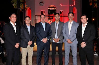 Seis hombres vestidos de traje posan con sonrisas en un ambiente iluminado con luces rojas durante el evento de Doppelherz.