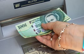 Una persona extrae un billete de cien mil guaraníes de un cajero automático.