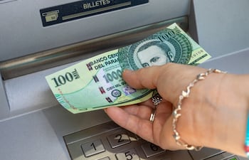 Una persona extrae un billete de cien mil guaraníes de un cajero automático.