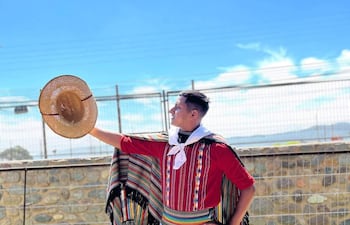 Brahian Barrios, vestido con camisa roja y poncho colorido, sostiene un sombrero mientras posa en un campo.