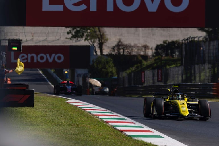 Automóvil de carreras amarillo y negro en la pista, con oficial de pista sosteniendo bandera amarilla.