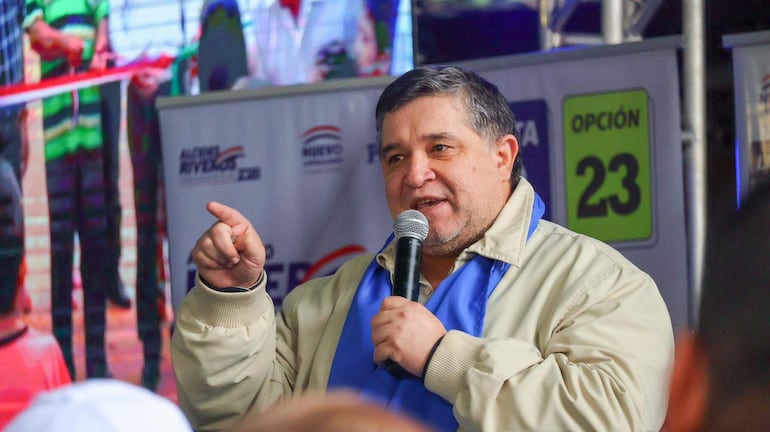 Alcides Riveros con micrófono en mano, gesticulando enérgicamente, rodeado de una multitud en un evento político al aire libre.