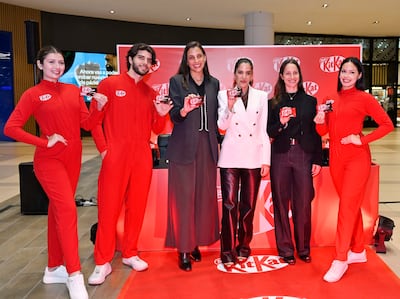 Cuatro personas en atuendos rojos y una en blanco, sosteniendo Kit Kat y sonriendo, en un ambiente decorado en rojo.