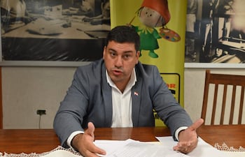 Diego Romero sentado en mesa de madera, vestido con saco gris y camisa blanca, gesticulando durante su discurso.