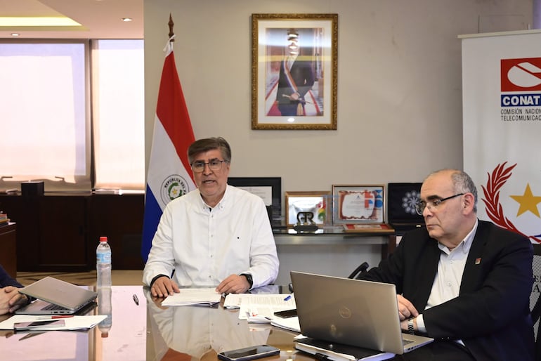 Juan Carlos Duarte en camisa blanca, hablando en reunión oficial con bandera de Paraguay y documentos sobre la mesa.