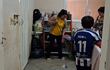 Mujer en camiseta amarilla y suéter claro limpia el suelo; niño de espaldas con camiseta de fútbol Oscar L. 11 observa.