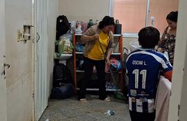 Mujer en camiseta amarilla y suéter claro limpia el suelo; niño de espaldas con camiseta de fútbol Oscar L. 11 observa.