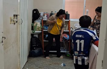 Mujer en camiseta amarilla y suéter claro limpia el suelo; niño de espaldas con camiseta de fútbol Oscar L. 11 observa.