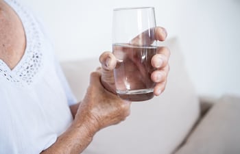 Una mujer con párkinson se ataja la mano para poder tomar un vaso de agua.