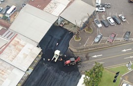 Vista aérea de trabajadores aplicando asfalto en una obra, rodeados de maquinaria pesada y vehículos en una calle urbana.