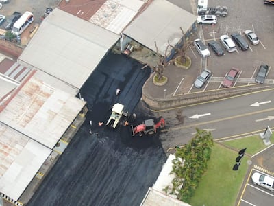 Vista aérea de trabajadores aplicando asfalto en una obra, rodeados de maquinaria pesada y vehículos en una calle urbana.