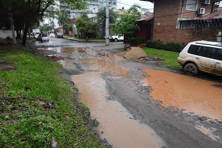 Calle inundada con vehículos, montículo de arena en la acera, vegetación a los lados en un día nublado.