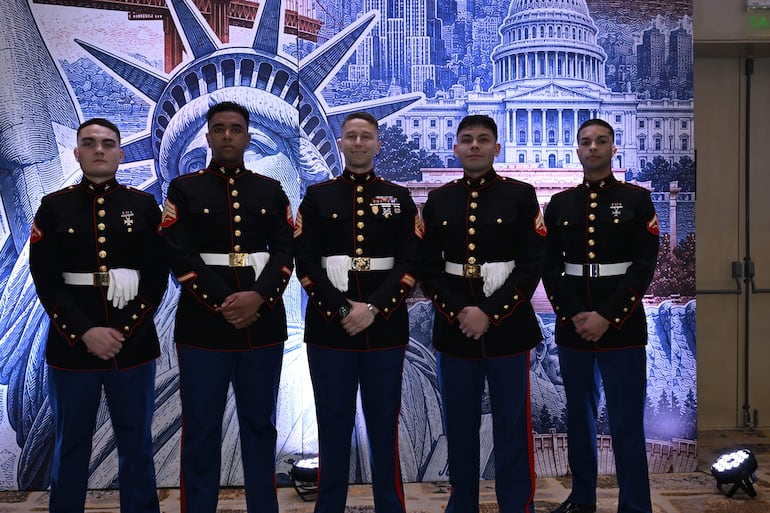 Cinco hombres en uniformes militares oscuros y azules se alinean, con la Estatua de la Libertad de fondo.