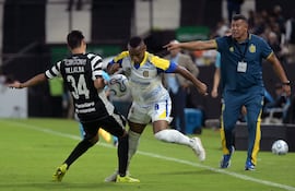 El defensor de Libertad Estiven Villalba y el mediocampista colombiano de Rosario Central Jaminton Campaz luchan por el balón ante la mirada del director técnico de Rosario Central, Jorge Almirón, durante el partido de fútbol de la fase de grupos de la Copa Libertadores.