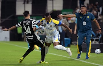El defensor de Libertad Estiven Villalba y el mediocampista colombiano de Rosario Central Jaminton Campaz luchan por el balón ante la mirada del director técnico de Rosario Central, Jorge Almirón, durante el partido de fútbol de la fase de grupos de la Copa Libertadores.