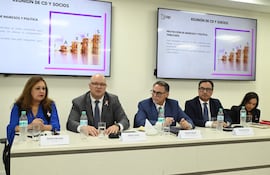 Óscar Lovera, calvo y con gafas, habla en reunión con Gerardo Ruiz Díaz y Teodora Recalde, todos con trajes formales y serias expresiones.