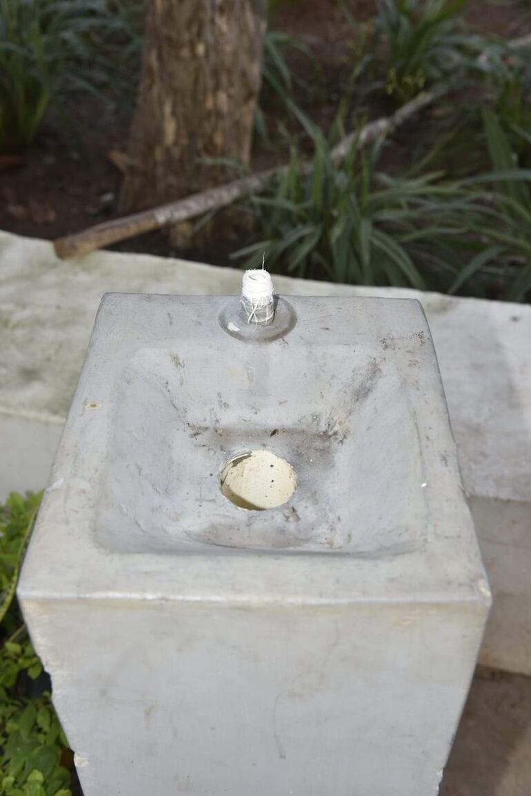 Lavabo de concreto gris en desuso, cubierto de suciedad, rodeado de vegetación en un entorno exterior.