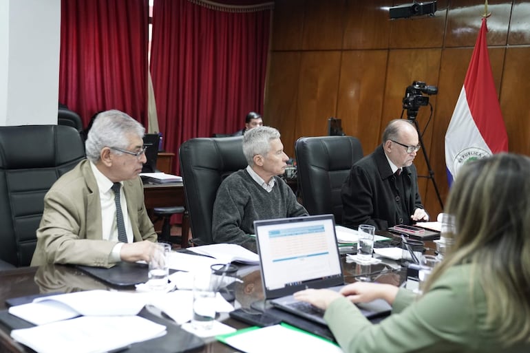 José Emilio Argaña Contreras con cabello canoso y gafas, escucha atento; José Jara Rojas en suéter gris y tres personas alrededor en reunión formal.