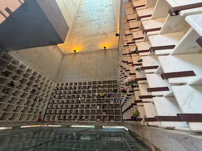 Interior del mausoleo minimalista con nichos de urnas, flores y luz suave resaltando el concreto.