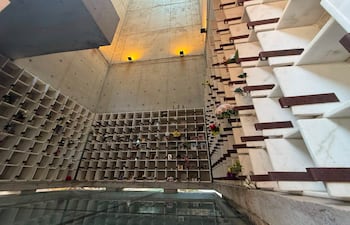 Interior del mausoleo minimalista con nichos de urnas, flores y luz suave resaltando el concreto.