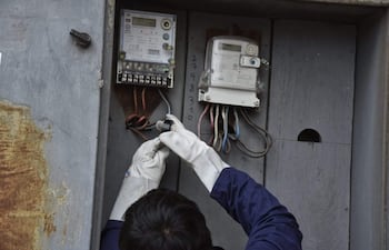 Funcionario en guantes blancos y chaqueta oscura trabaja en panel eléctrico con medidores desconectados en un entorno exterior.
