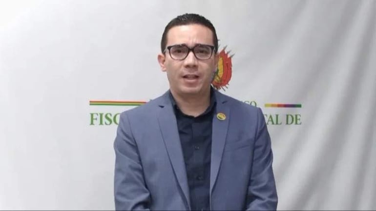 Alberto Zeballos Flores, hombre de cabello corto, en chaqueta gris claro, hablando a la cámara frente a fondo institucional.