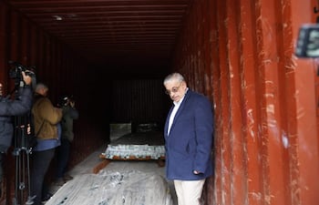 Isaías Fretes con chaqueta oscura y camisa blanca, observa el interior de un contenedor, rodeado de fotógrafos en un ambiente de inspección.