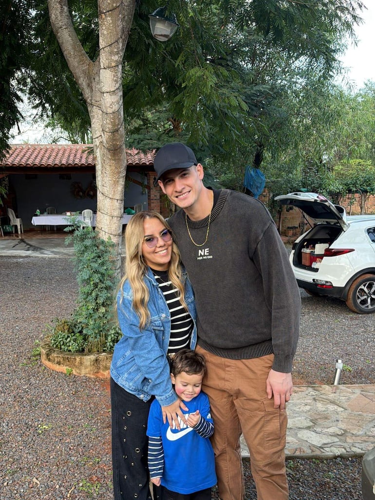 Orlando Gill, mujer rubia con chaqueta de mezclilla y niño en camiseta azul sonríen en un jardín soleado.