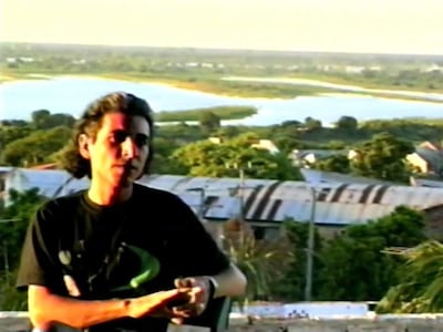 Feliciano Centurión sentado, gesticulando con camiseta oscura y cabello largo en un paisaje natural junto al río.