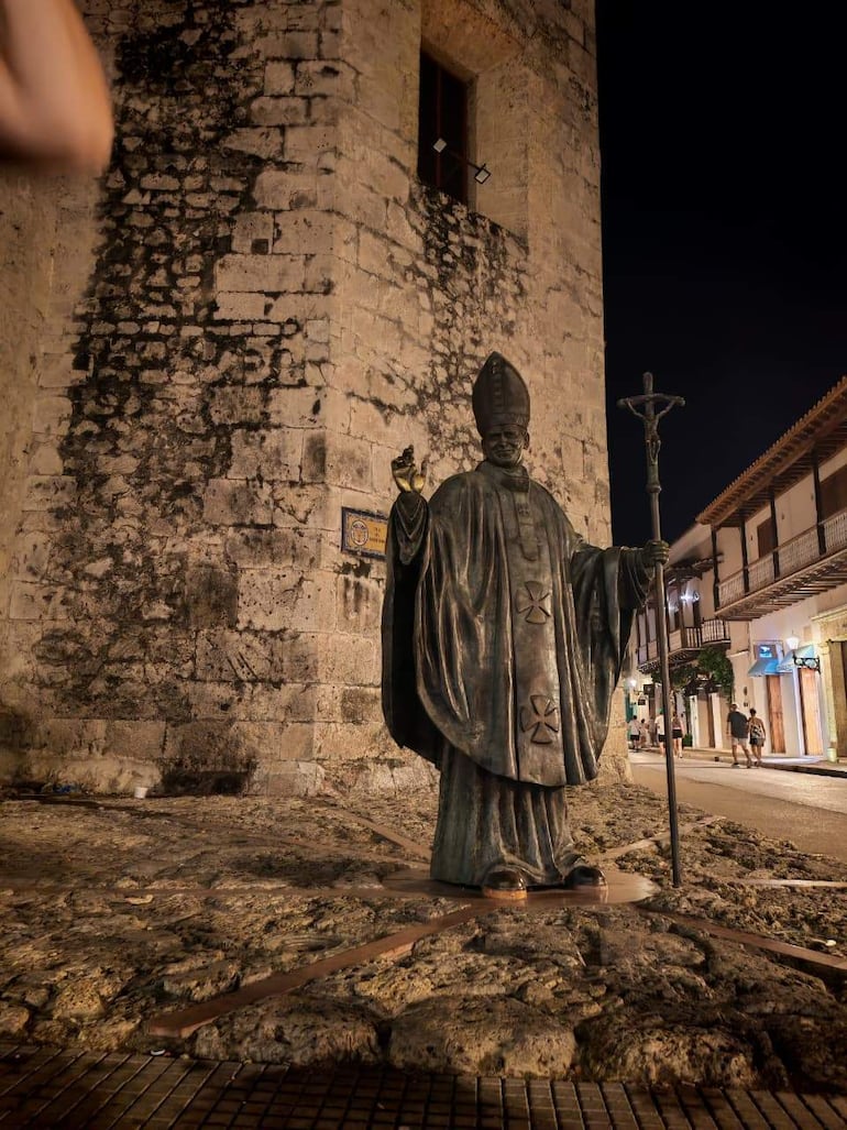 Estatua de un religioso en pedestal, iluminada tenuemente en calle coloniales de Cartagena, sin personas visibles.