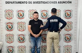 Esteban David Benítez Meaurio, vestido con camiseta negra y jeans, es sostenido por un oficial en estación policial.