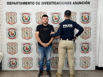 Esteban David Benítez Meaurio, vestido con camiseta negra y jeans, es sostenido por un oficial en estación policial.