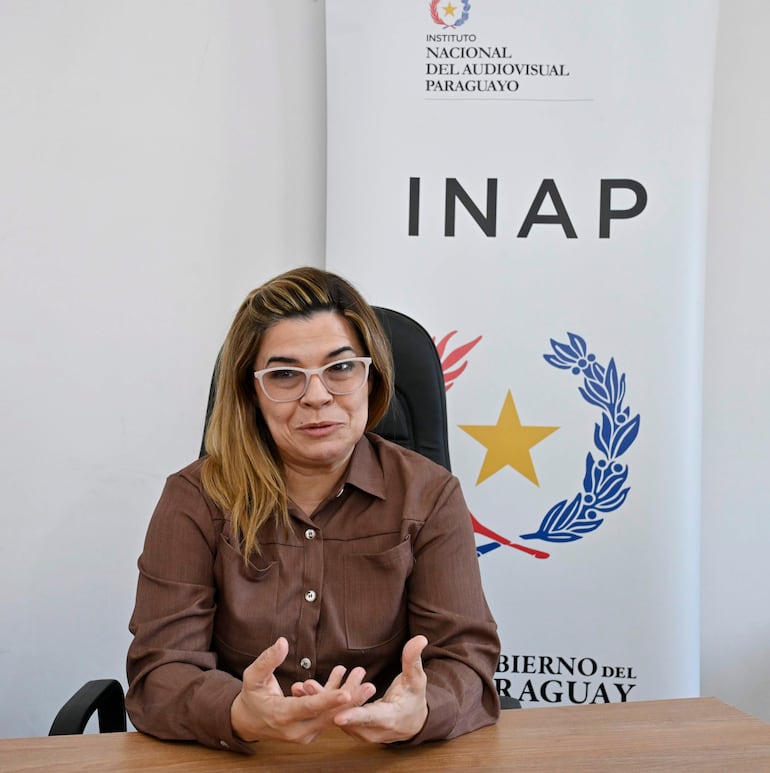 Natalia Fuster, mujer con blusa marrón y gafas, habla gesticulando en un entorno profesional con logotipos del INAP.