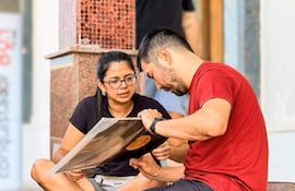 Mujer con camiseta negra y hombre con camiseta roja observan un disco de vinilo sentados en una escalera.