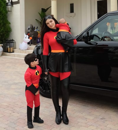 Nadia Ferreira en disfraz rojo y negro, con dos niños disfracecidos, en un ambiente festivo con decoraciones de Halloween.