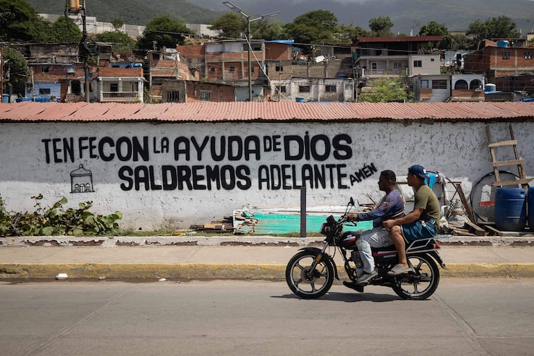 Personas transitan en una moto frente a un mural, en Catia La Mar (Venezuela). 